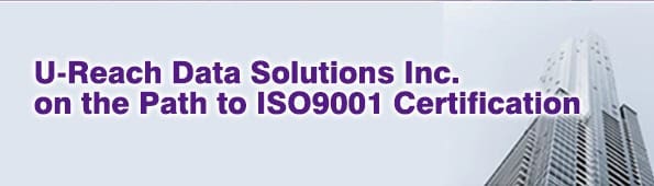 A banner with the text U-Reach Data Solutions Inc. on the Path to ISO9001 Certification in purple, next to a tall, modern office building seen from below.